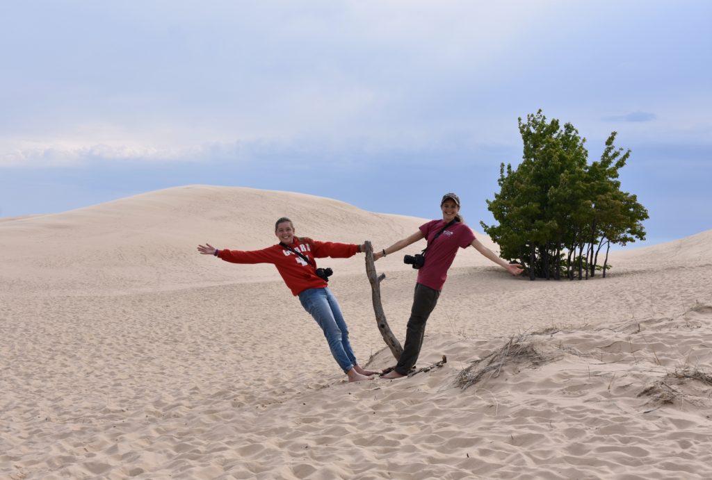 Explore Michigan Lighthouses & Sand Dunes. Two girls holding on to a stick on huge sand dunes.