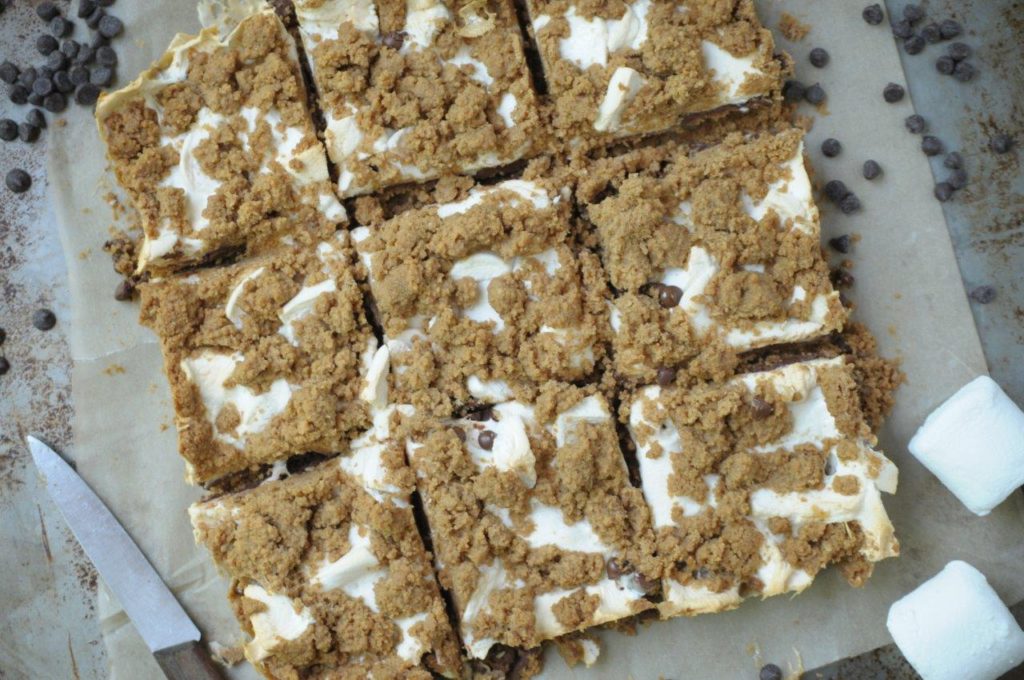 Gluten free s'more bars.  S'more bars cut and setting on a baking sheet with a knife, mini chocolate chips and marshmallows.