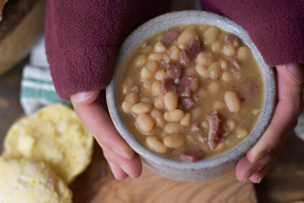 Classic Ham and Bean Soup.  A lady holding a bowl of warm bean soup.