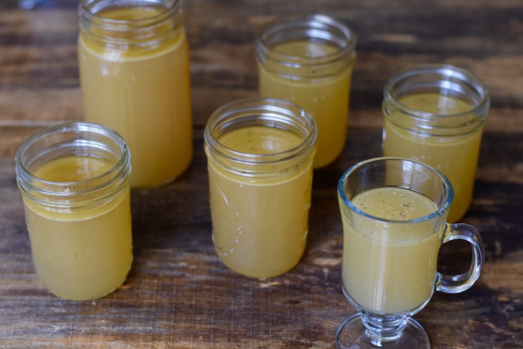 Homemade Chicken Broth in canning jars setting on a wooden table.
