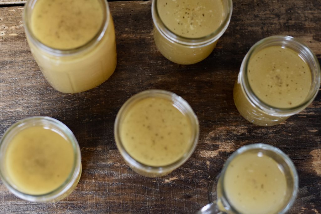 Homemade Chicken broth in jars set on a wooden table.