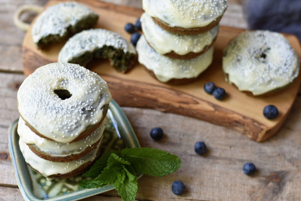 Grain Free blueberry doughnuts stacked on a small board with random blueberries.