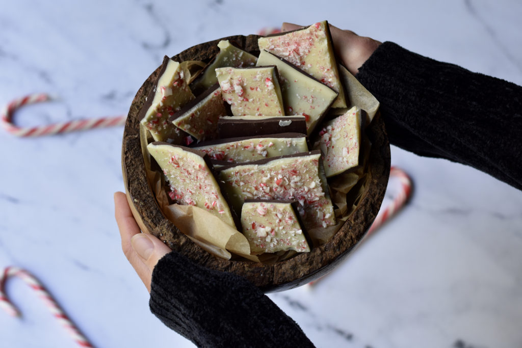 A person holding a bowl of gluten free white chocolate peppermint bark.