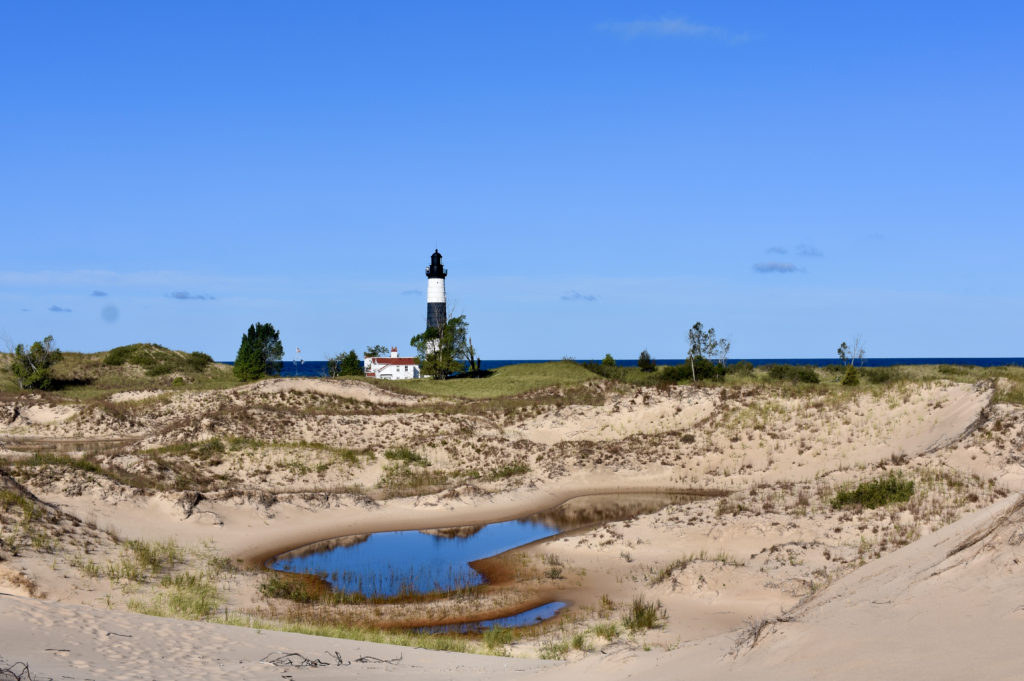 A black and white lighthouse sitting among sand dunes by Lake Michigan.  The title is hiking in Ludington State Park, Michigan.
