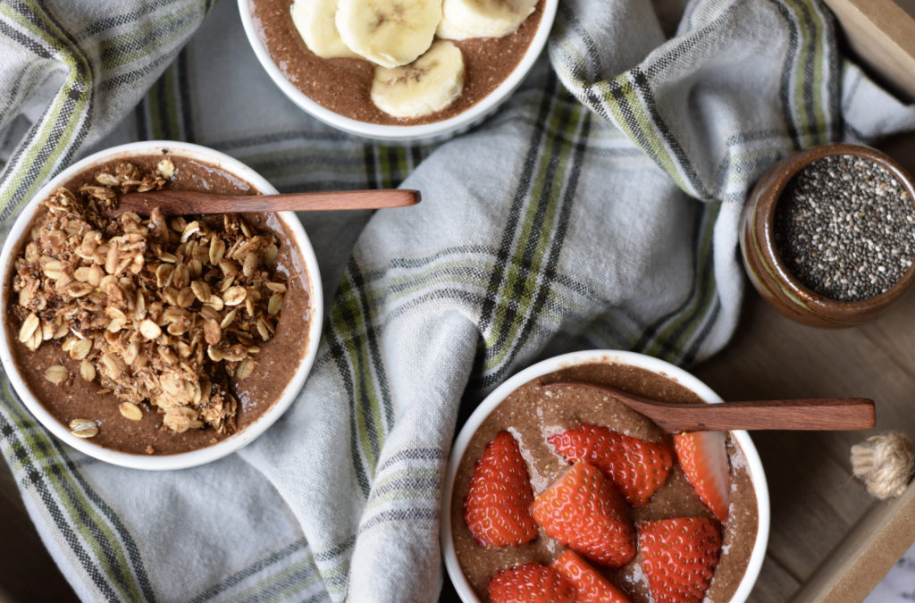 Two white bowls of chia pudding one with granola on top and the other with strawberries on top