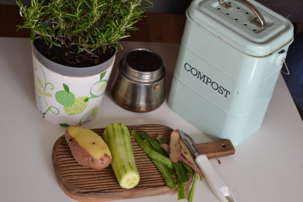 Vegetable scraps on a cutting board next to a stainless steel compost pot. Composting is one way to a sustainable home.