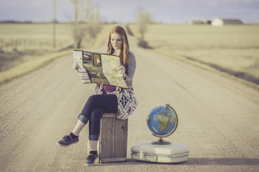 How to prepare for travel with food allergies with a women sitting on a suitcase reading a map.