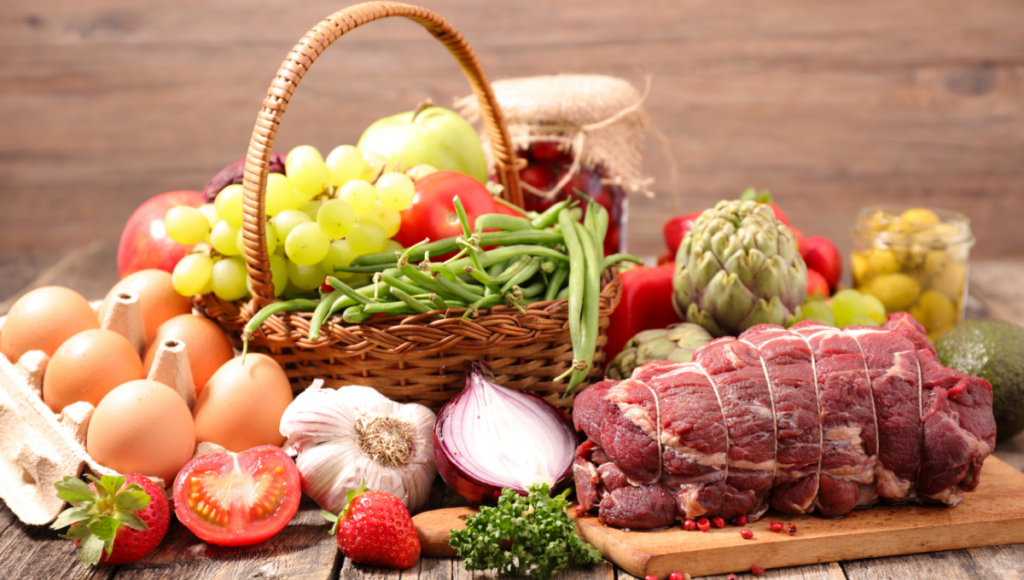 An assortment of food on a table, vegetables, fruit, meat and eggs.