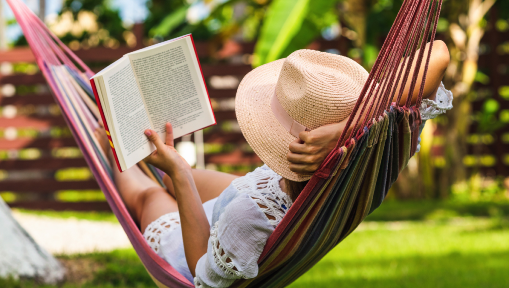 Improve your health and take a vacation.  A women relaxing in a hammock while reading a book.