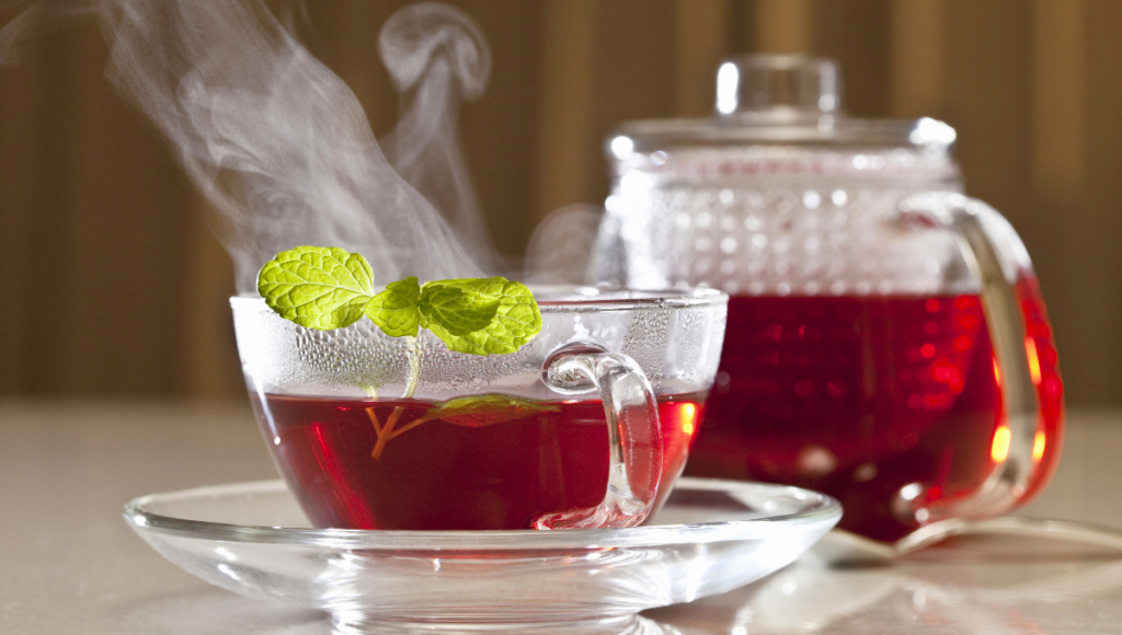 Ease Your Cold Symptoms with Herbal Teas. A red steaming tea mug with a peppermint leaf hanging out.