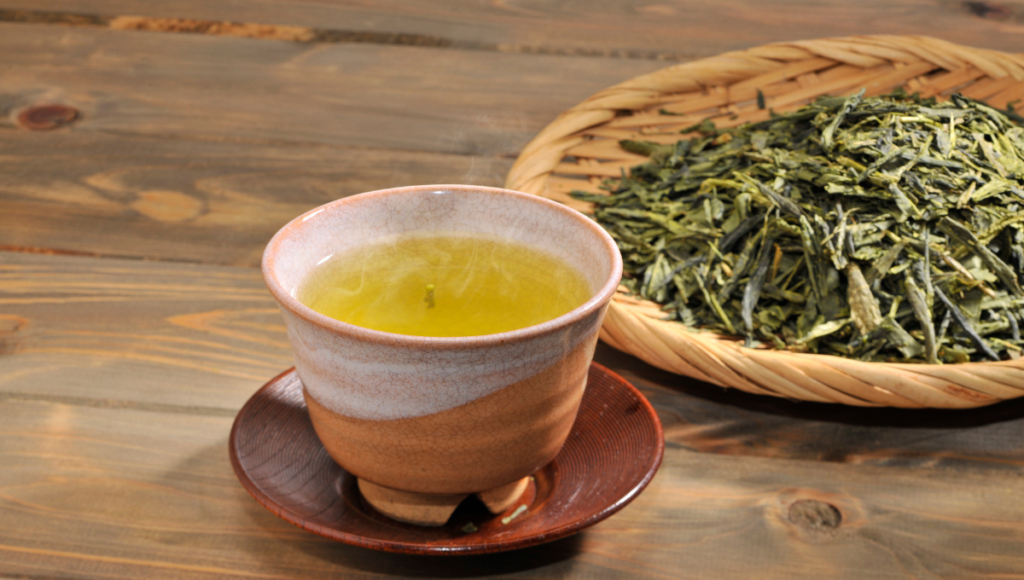 Why is green tea good for me?  A cup of hot tea in a small mug with a basket of loose leaf green tea.